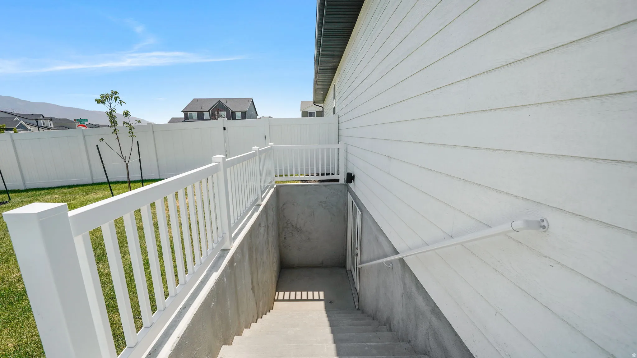 White vinyl fencing, concrete foundation, white exterior siding, and concrete basement stairwell