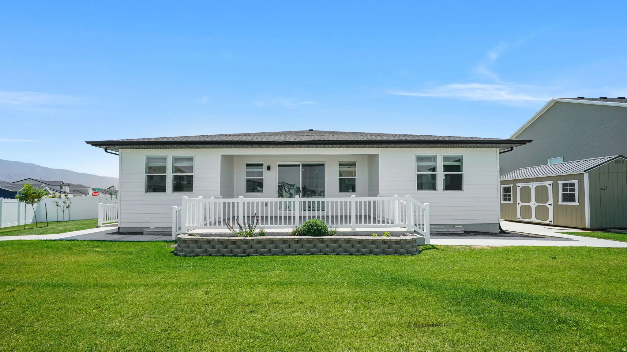 Back yard features an expansive green lawn with a white fenced patio and a built-in planter