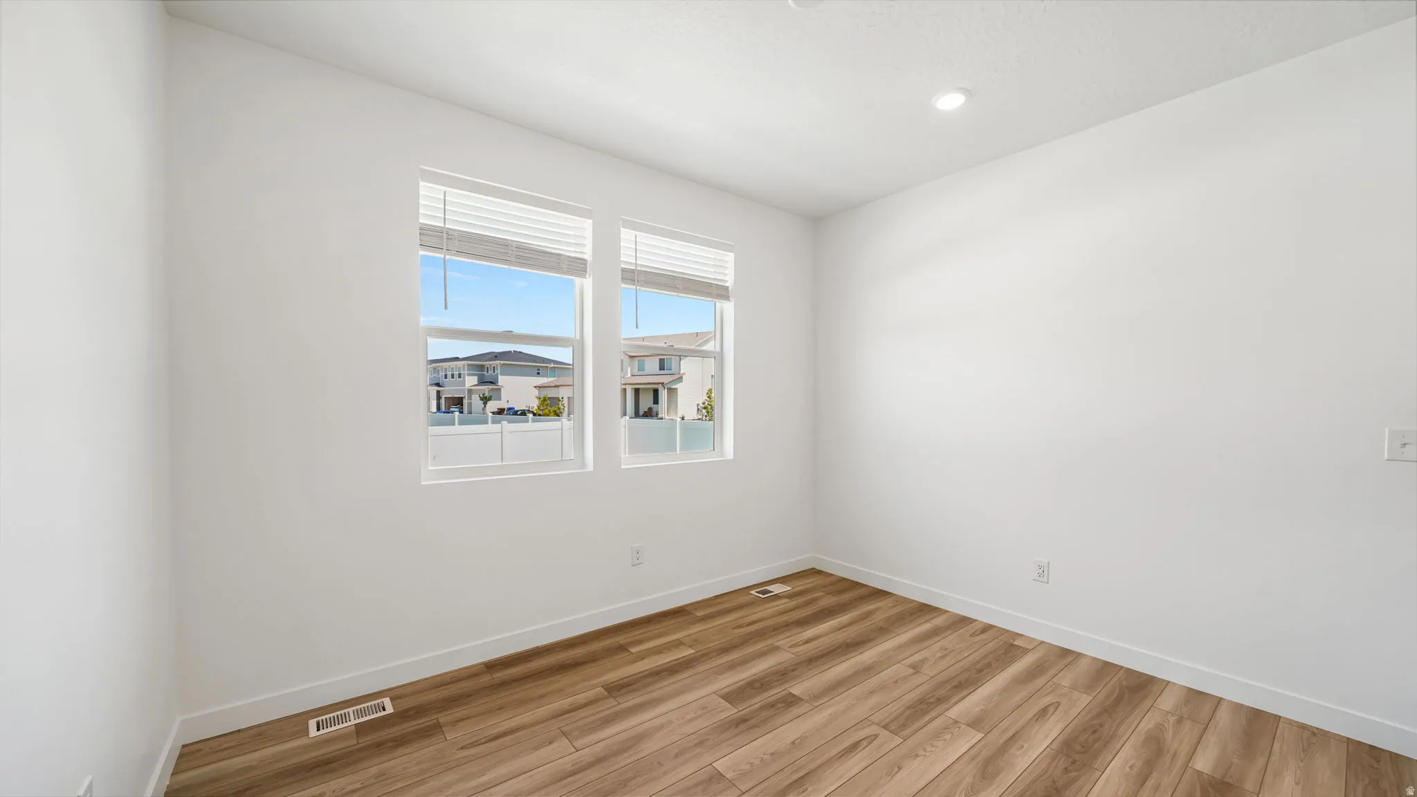 Bright room with two large windows, wood-finish flooring, recessed lighting, and crisp white walls