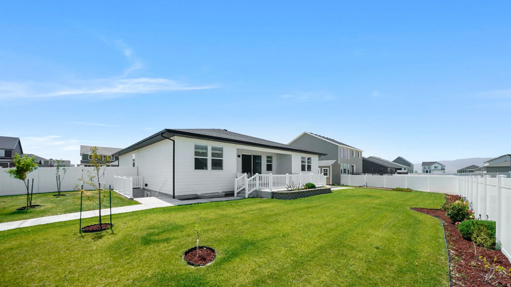 Expansive backyard featuring a manicured lawn, white vinyl fencing, a raised deck, and landscaping beds