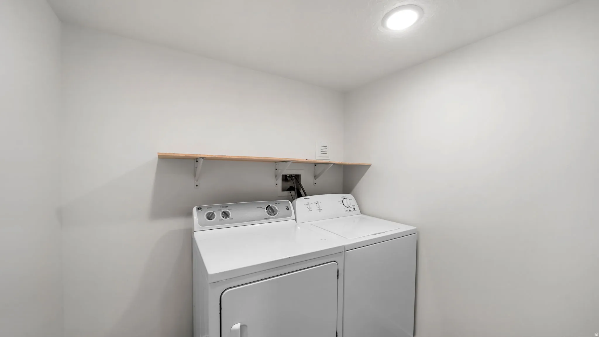 Laundry appliances with a wood-finish shelf and overhead lighting