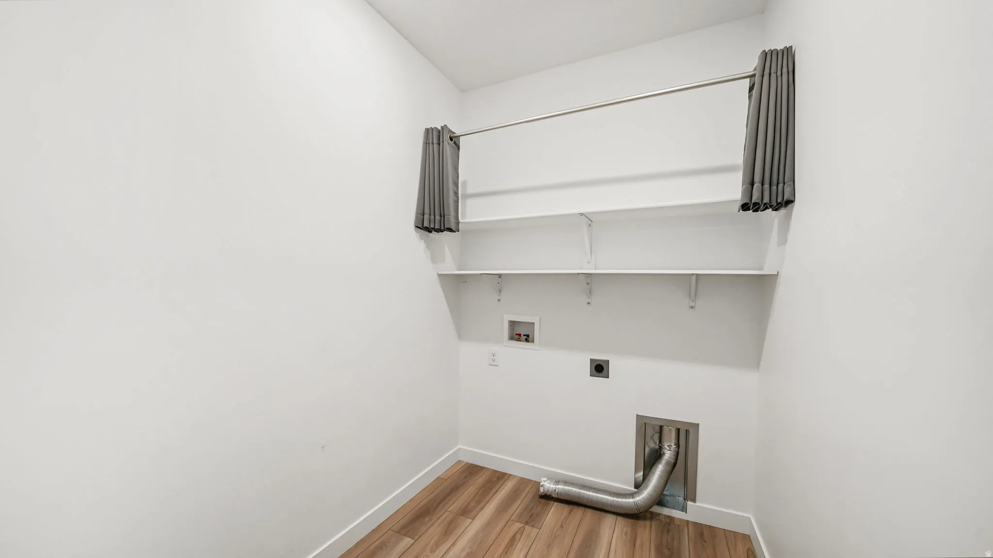 Laundry area featuring wood-finish flooring, two wall-mounted shelves, and a 220v electrical outlet for a dryer