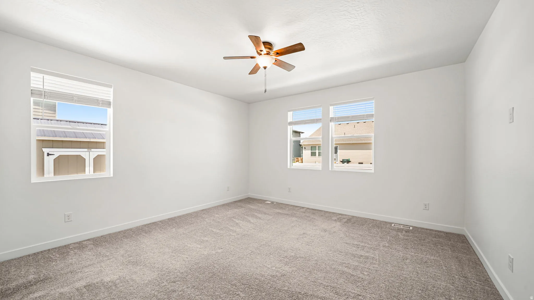 Large primary bedroom with carpeted flooring, white walls, multiple windows, ceiling fan with light fixture
