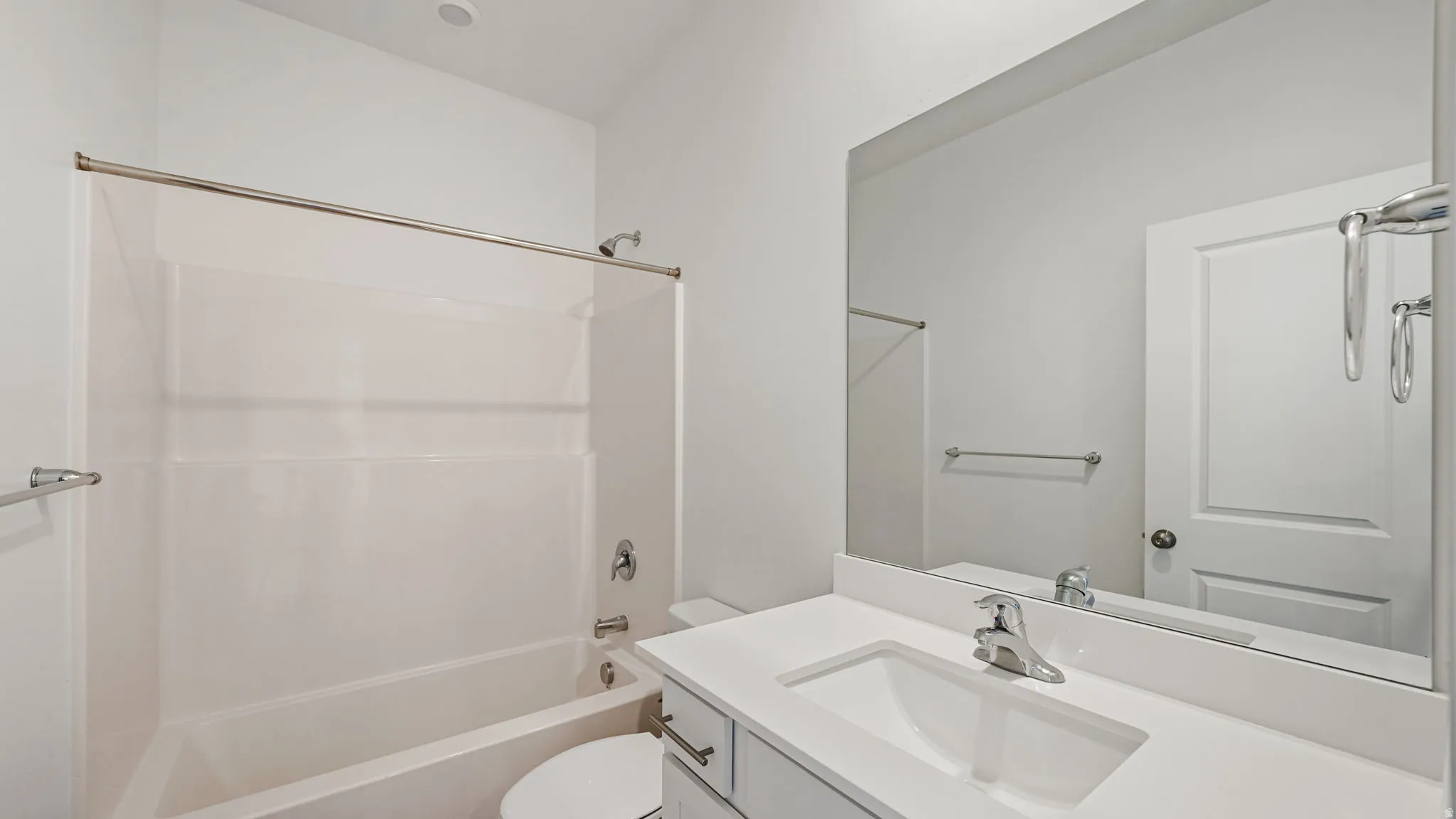 Integrated tub and shower combination, vanity with an integrated sink, polished chrome faucet, and a large wall-mounted mirror