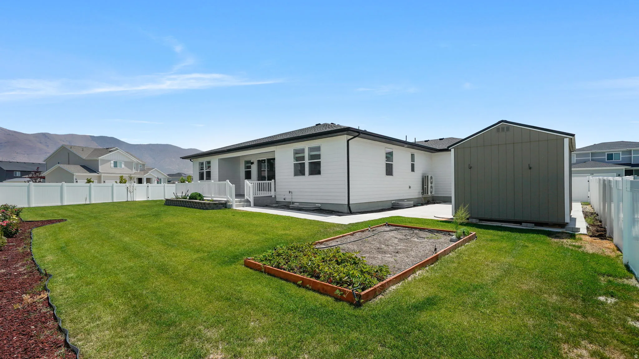 Expansive lawn with a raised garden bed, concrete patio, and white vinyl fencing