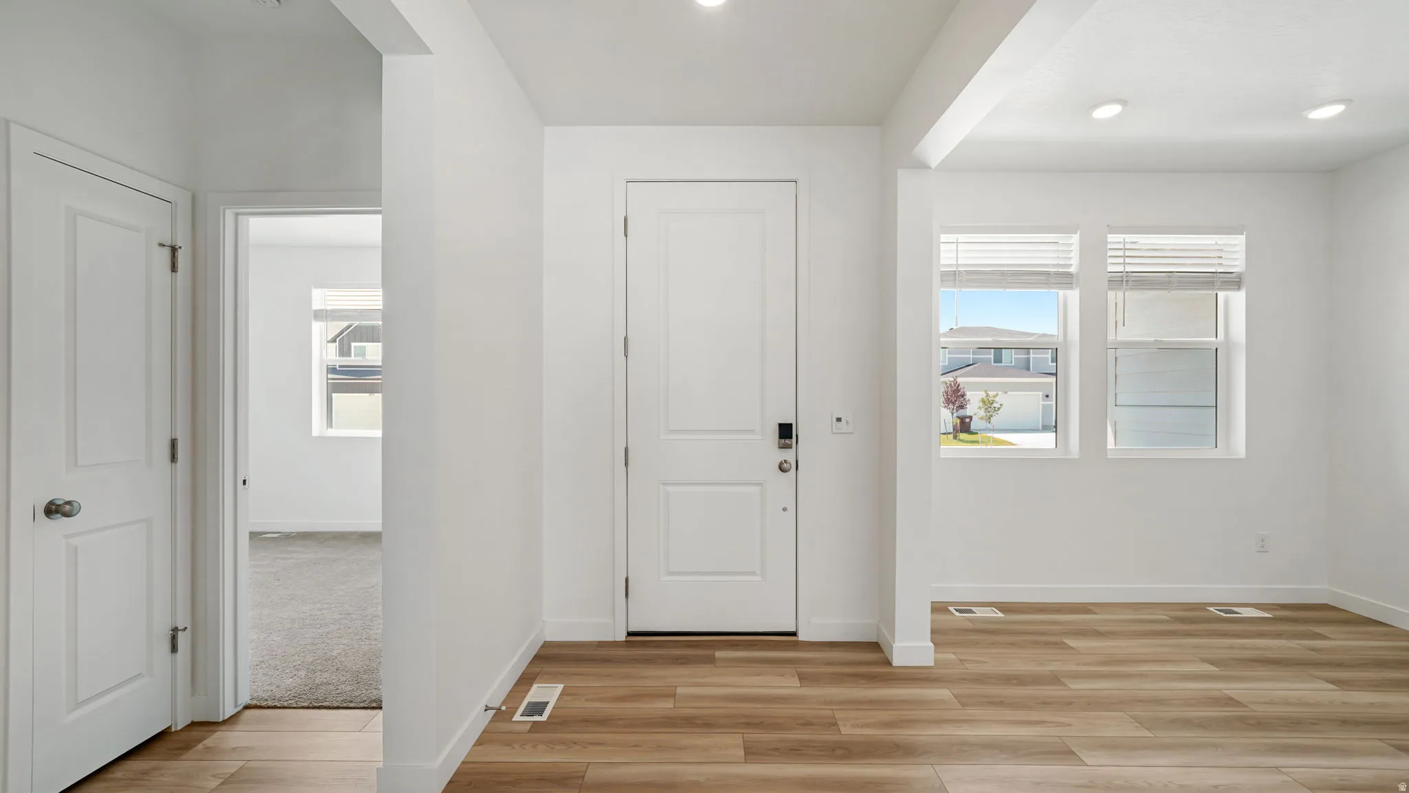 Wood-finish flooring, recessed lighting, and white trim throughout. A bedroom on the left and formal living room on the right.