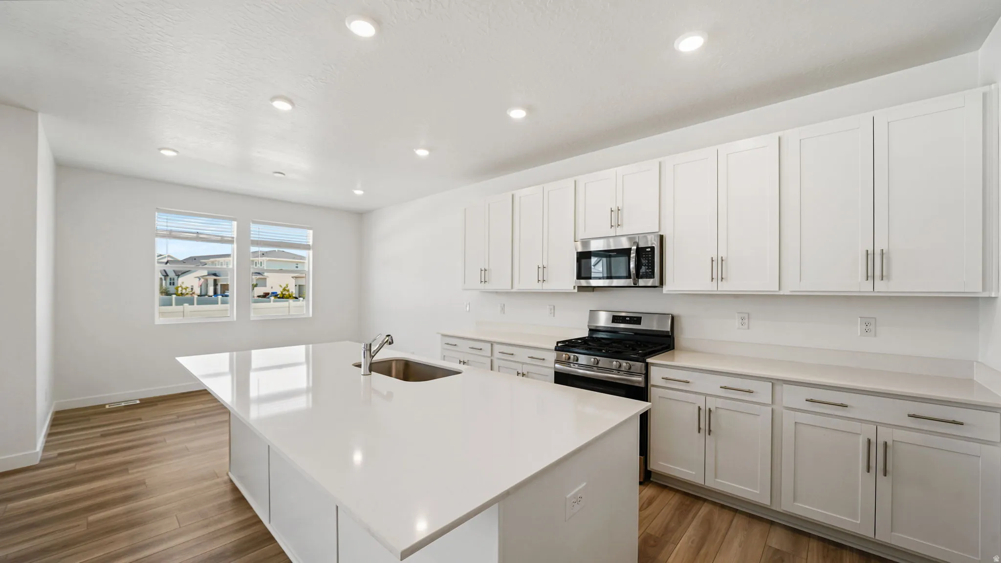 Modern kitchen featuring wood-finish flooring, white cabinetry, integrated stainless steel appliances, a center island with an undermount sink, and recessed lighting
