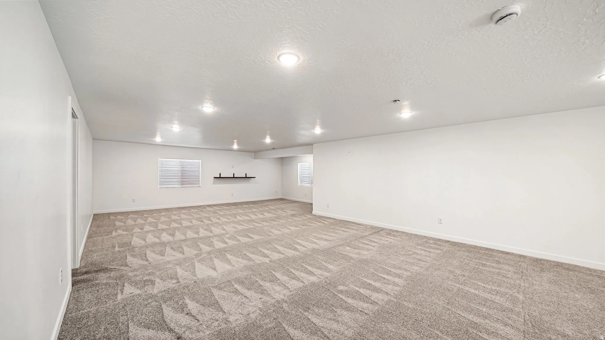 Spacious room featuring patterned carpet, recessed lighting, white walls, and a window with blinds