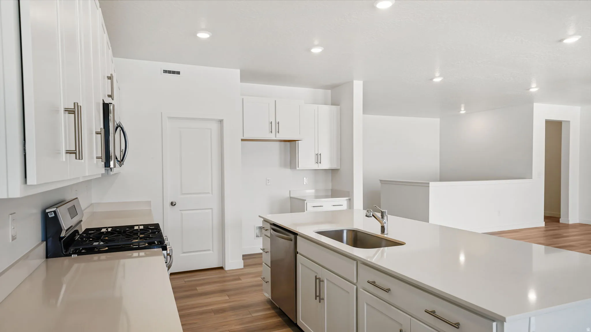 Kitchen featuring white cabinetry, light-toned countertops, a stainless steel sink, a built-in range, and wood-finish flooring