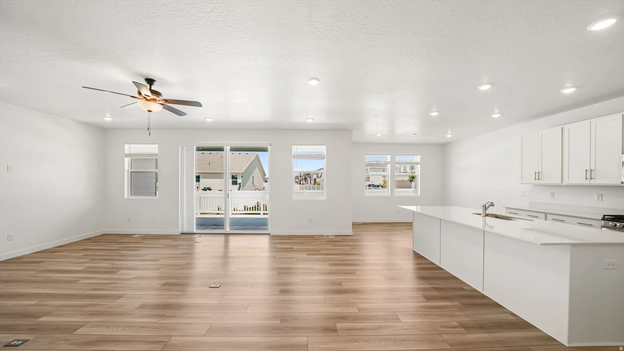 Open concept living area featuring wood-finish flooring, recessed lighting, a ceiling fan, sliding glass door, and a kitchen with white cabinetry and an expansive island