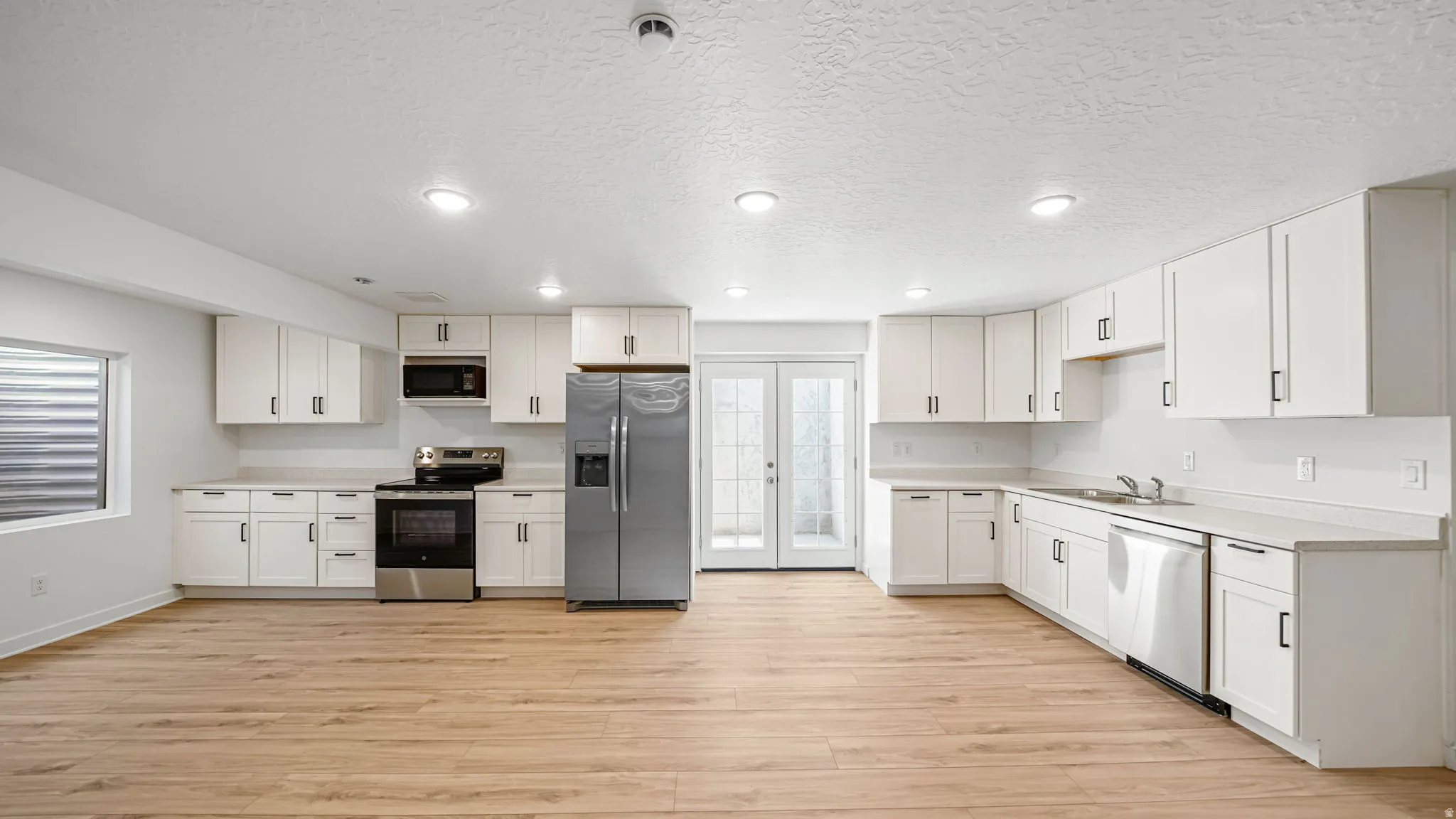 Expansive open-concept kitchen and dining area featuring white cabinetry, stainless steel appliances, and light-toned wood-finish flooring. Private entrance to basement ADU.