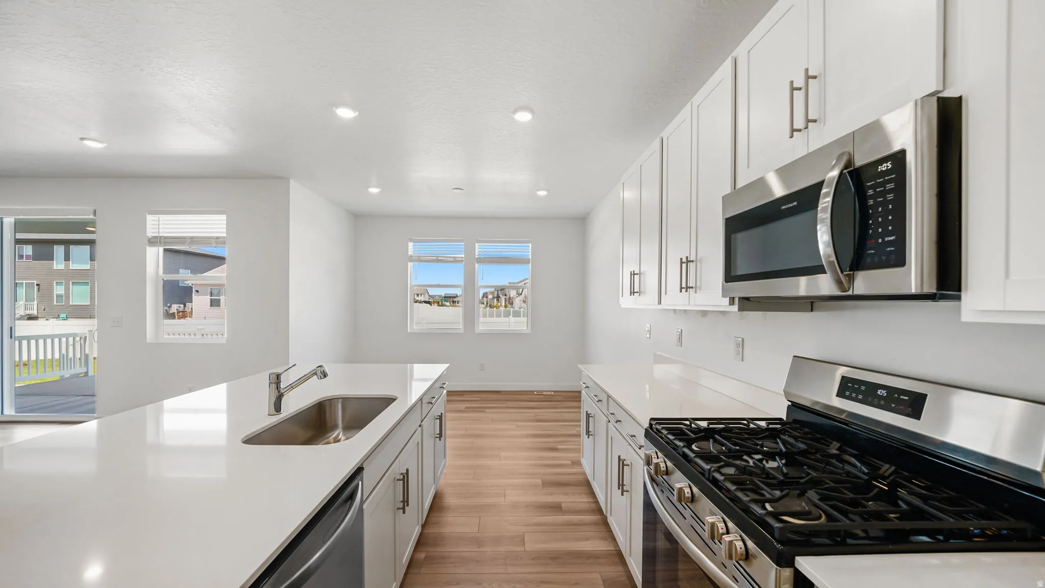 White cabinetry with stainless steel hardware, stainless steel appliances, wood-finish flooring, recessed lighting, and a kitchen island with an undermount sink
