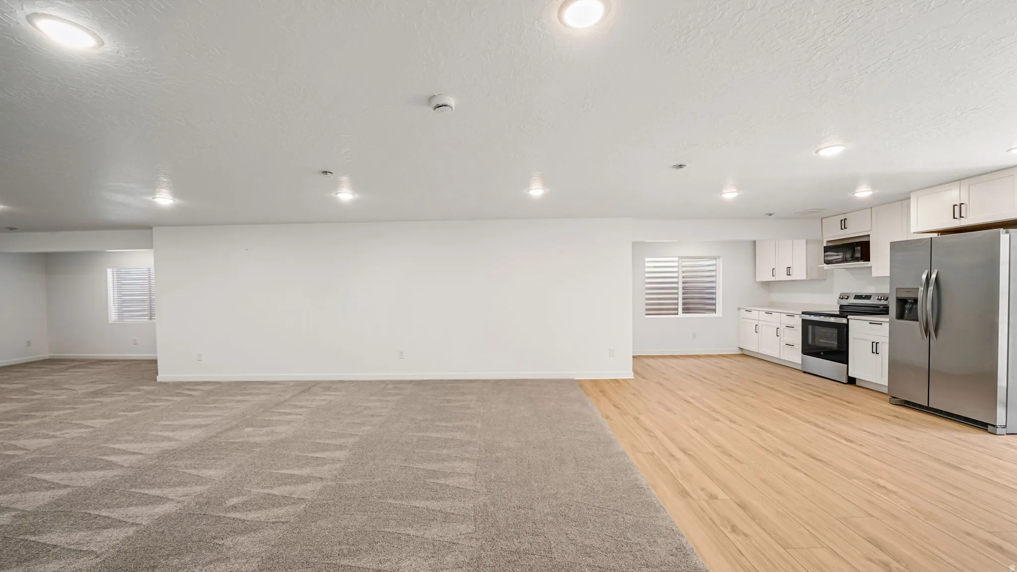 Recessed lighting, wood-finish flooring, stainless steel appliances, white cabinetry, and a patterned carpet