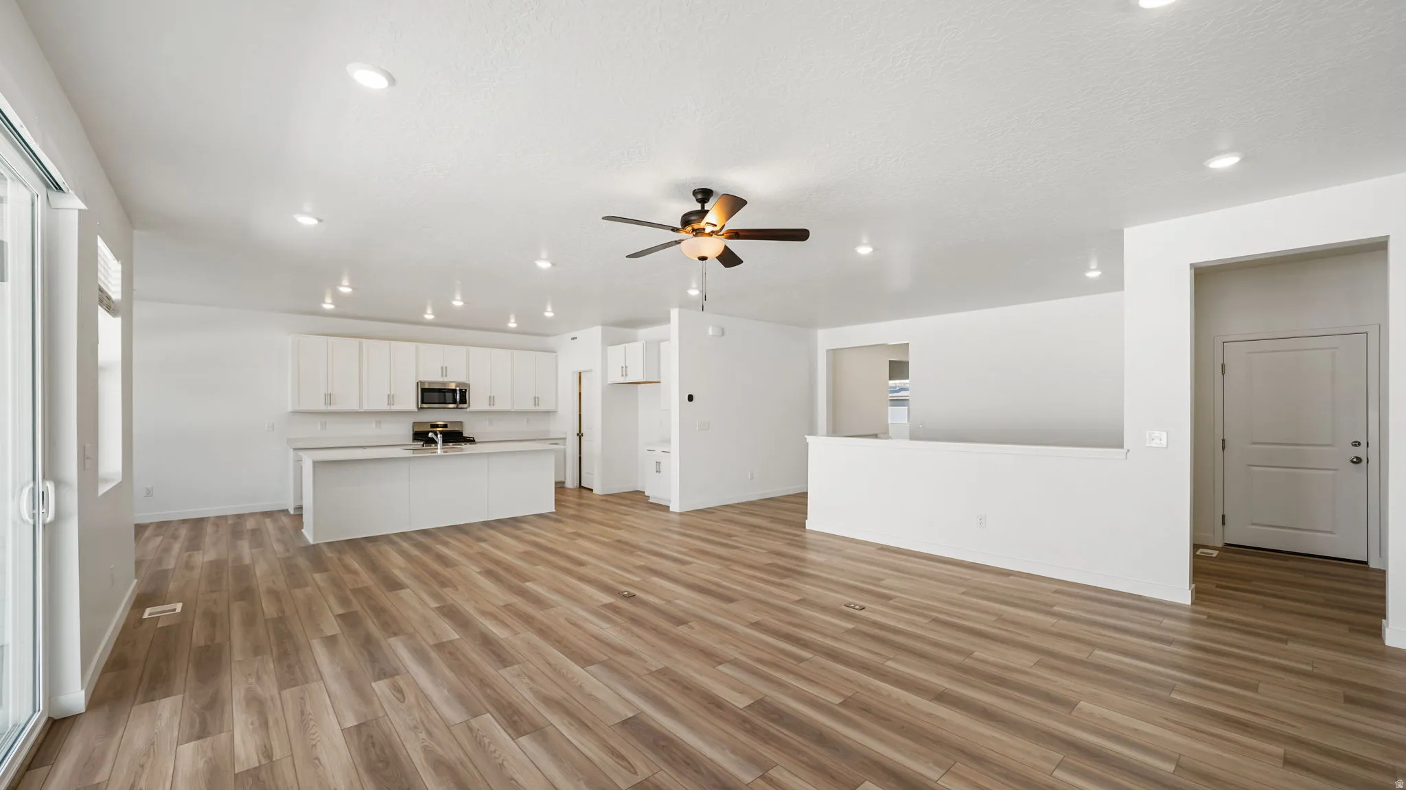 Wood-finish flooring throughout, recessed lighting, and a ceiling fan. Includes view to the garage door and mudroom and laundry