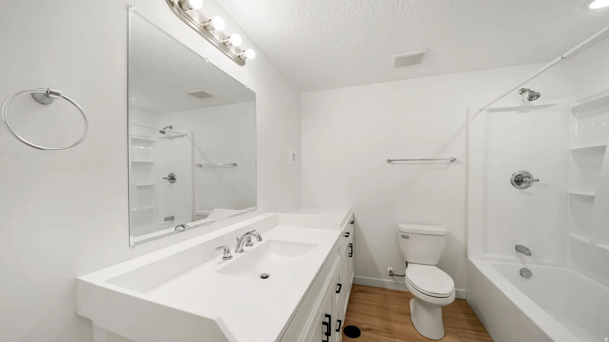 Dual vanity with integrated sink, wood-finish flooring, mirror, and a tub/shower combination