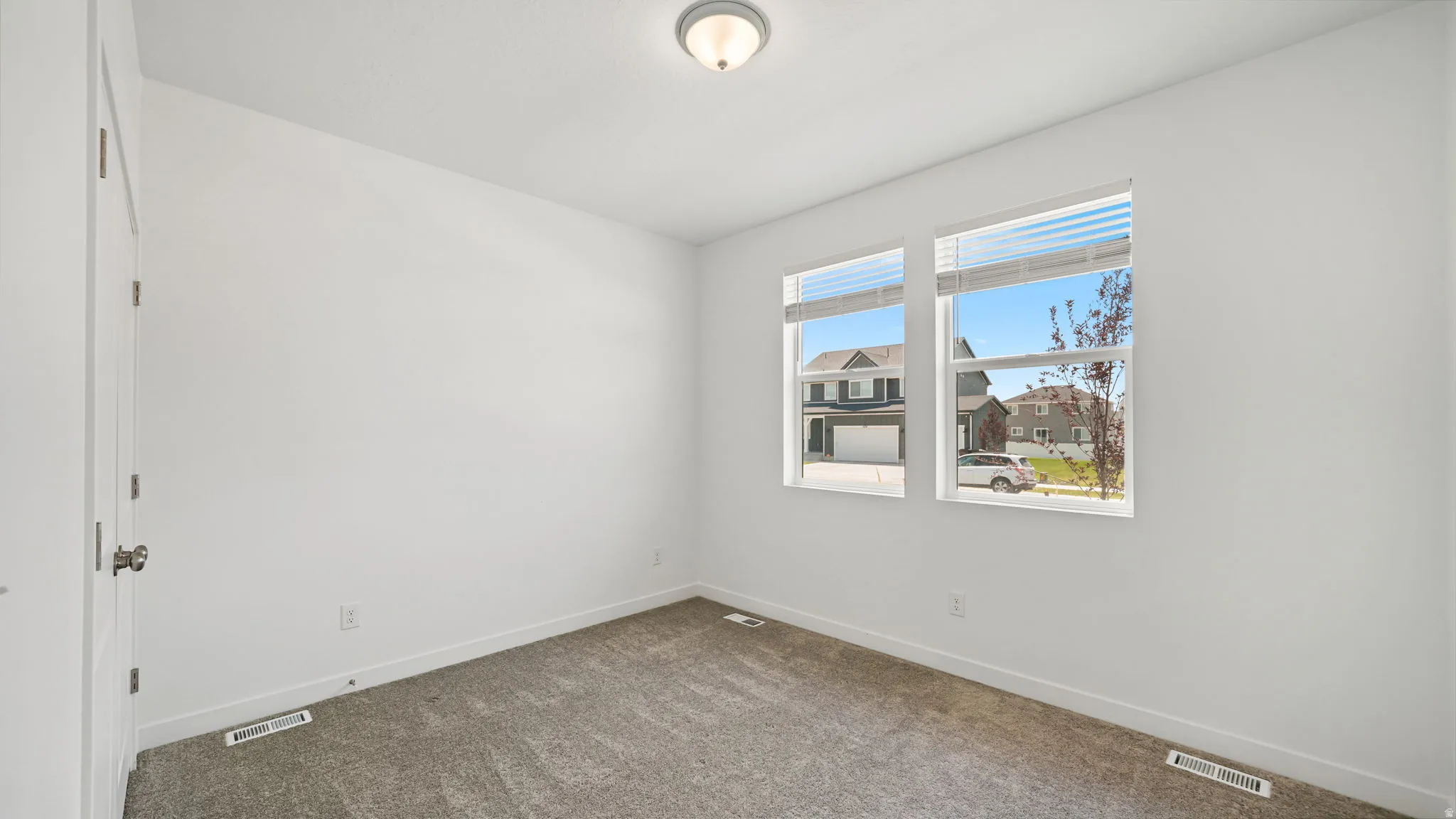 Neutral white walls, plush carpeting, two windows with blinds, and a semi-flush mount ceiling light