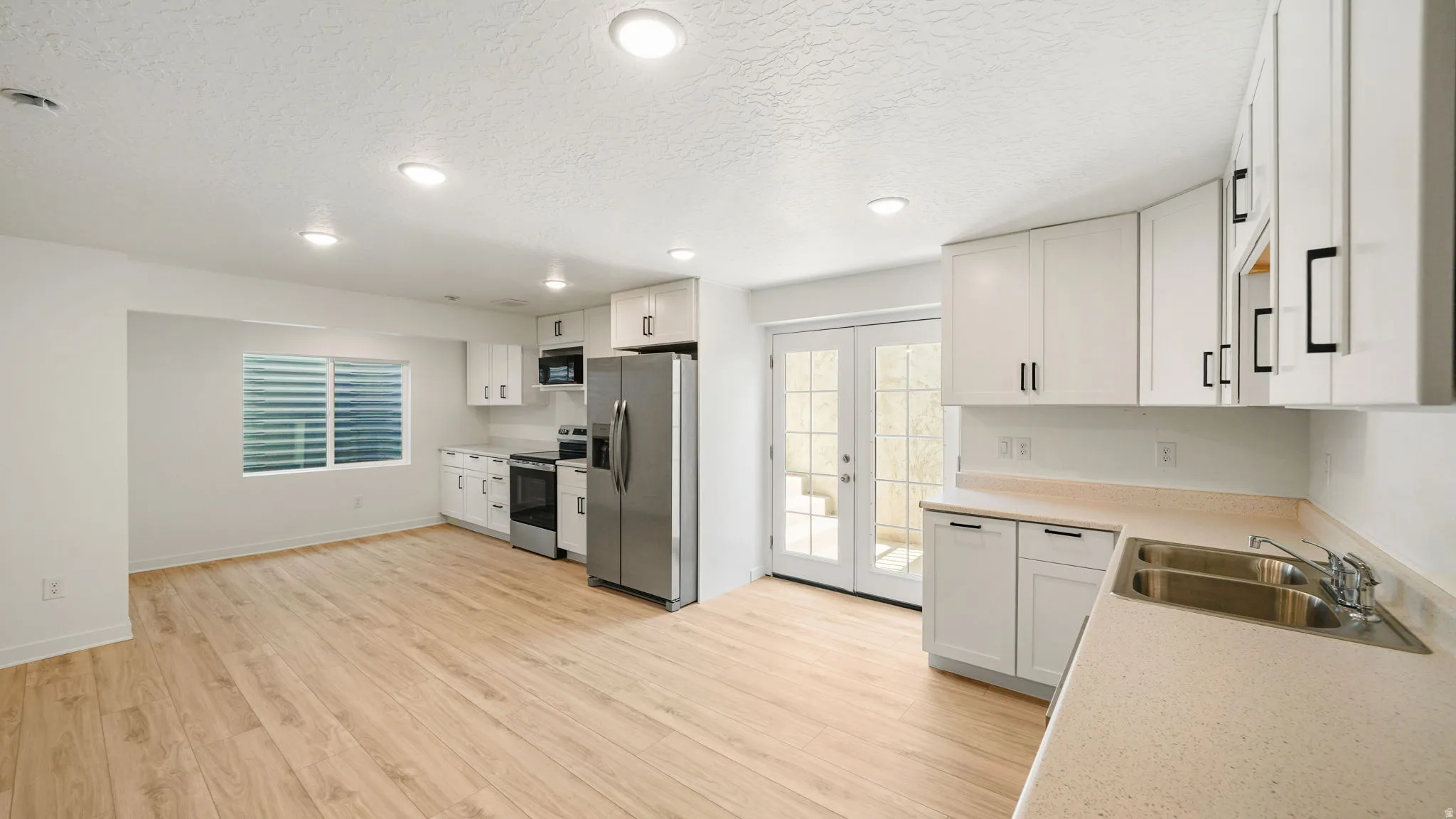 Open-concept living area featuring wood-finish flooring, white cabinetry, stainless steel appliances, and a double basin sink