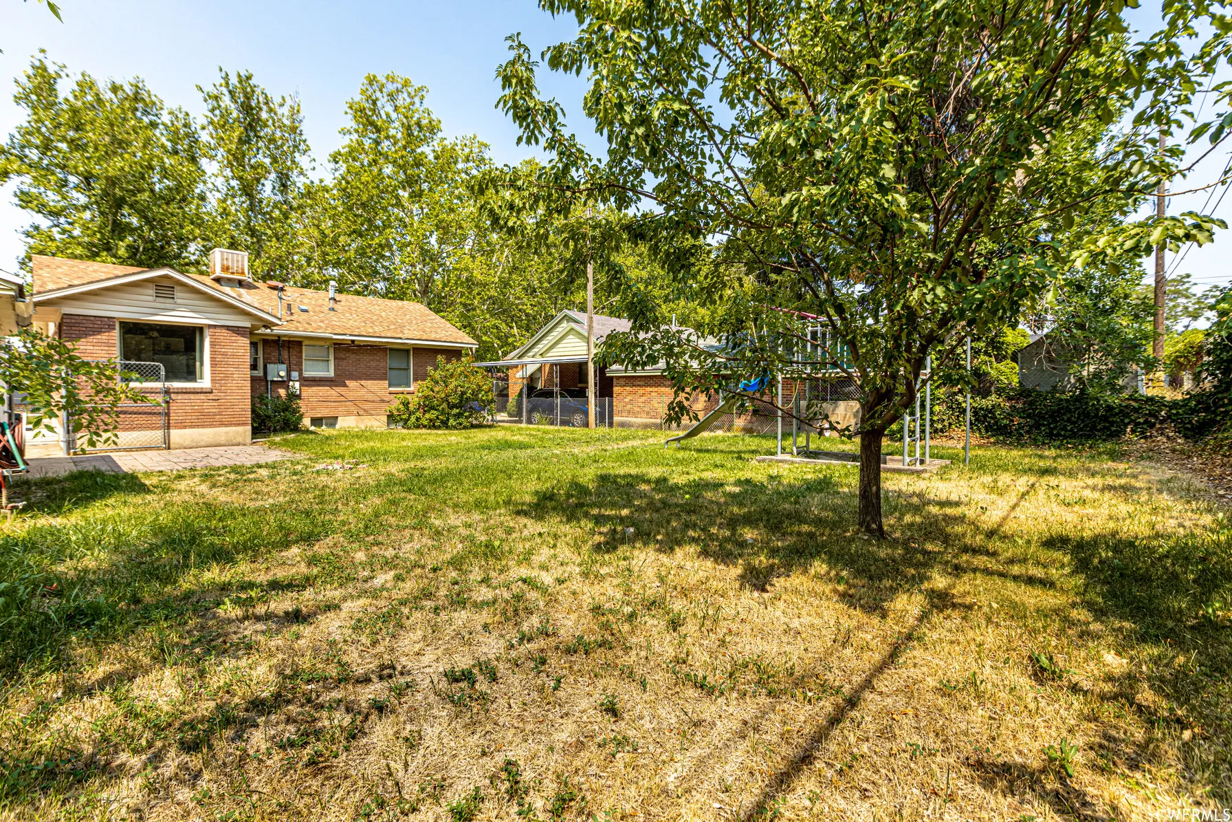 Expansive backyard featuring mature trees, a brick-clad exterior, and a paved patio area