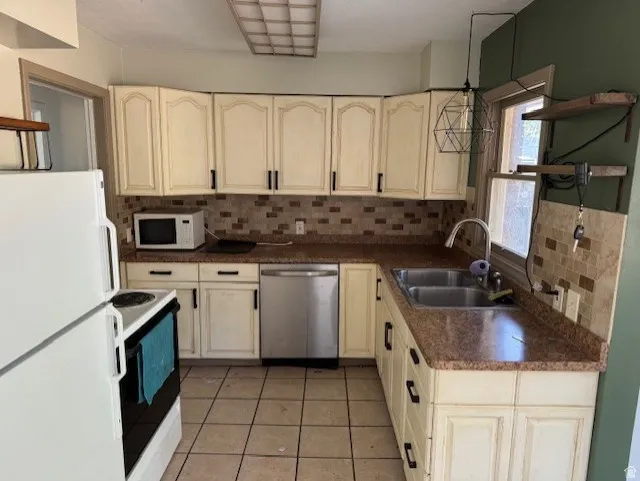 U-shaped kitchen layout featuring light-toned cabinetry, a mosaic tile backsplash, durable countertops, and a dual basin stainless steel sink