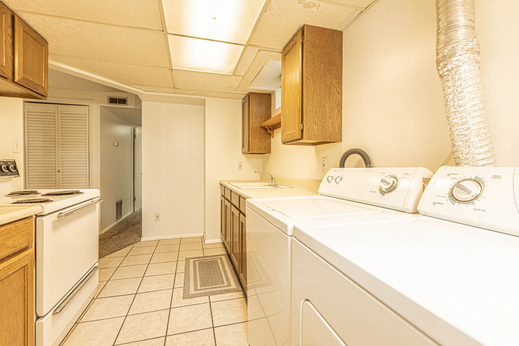 Built-in cabinetry, tile flooring, white appliances, and a drop ceiling with recessed lighting