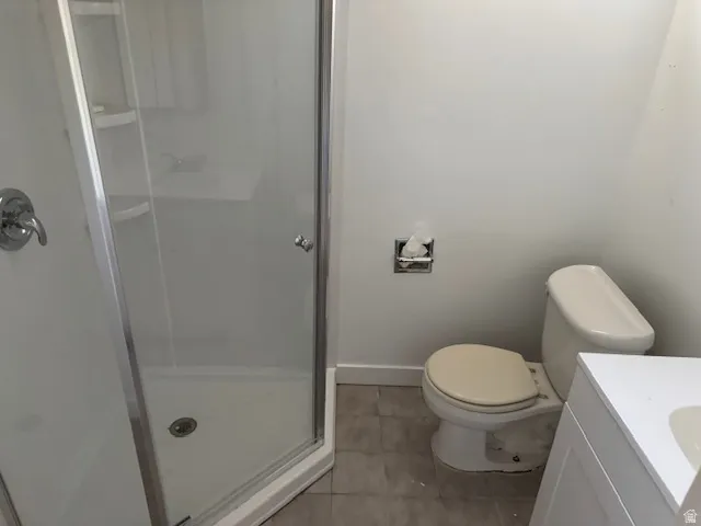 Glass-enclosed shower with chrome fixtures, white toilet, and tile flooring