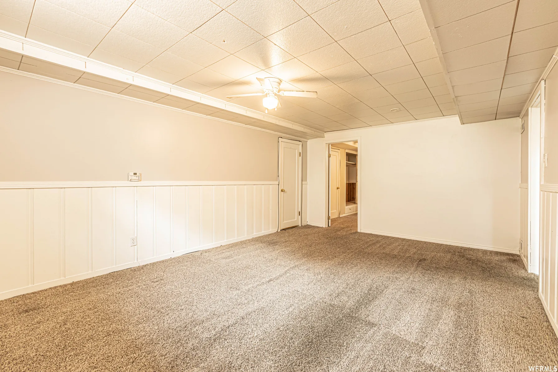 Carpeted flooring with wainscoting, a drop ceiling, and a ceiling fan with light fixture