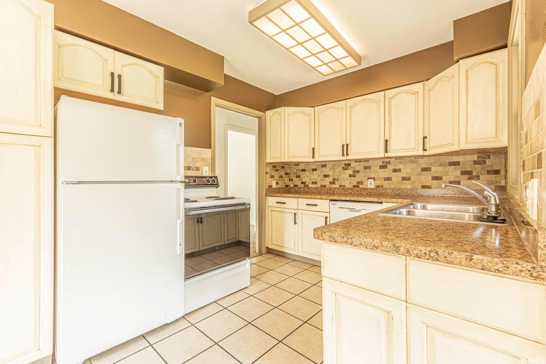 Kitchen featuring cream-colored cabinetry, laminate countertops, a tile backsplash, and a double basin stainless steel sink