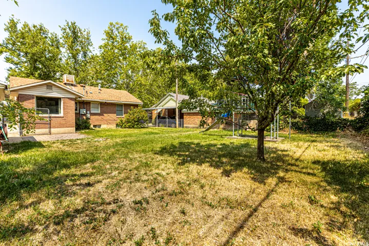 Expansive backyard featuring mature trees, a brick-clad exterior, and a paved patio area