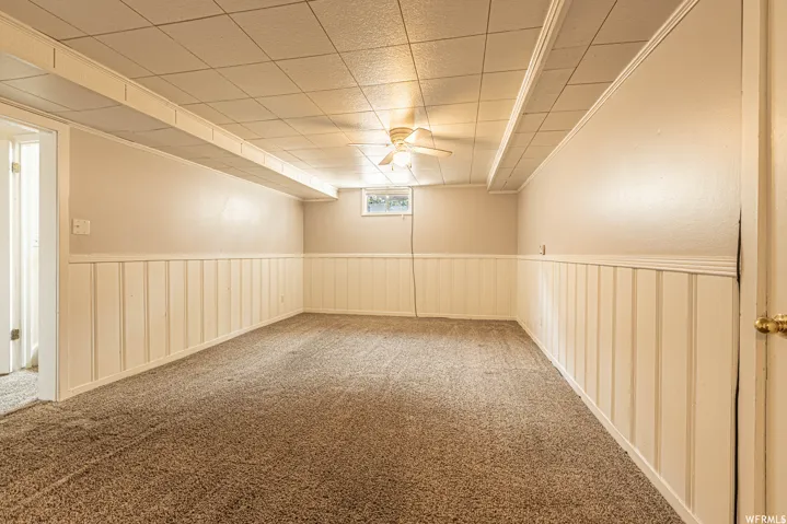 Expansive room featuring carpet flooring, wainscoting, and a drop ceiling with integrated lighting