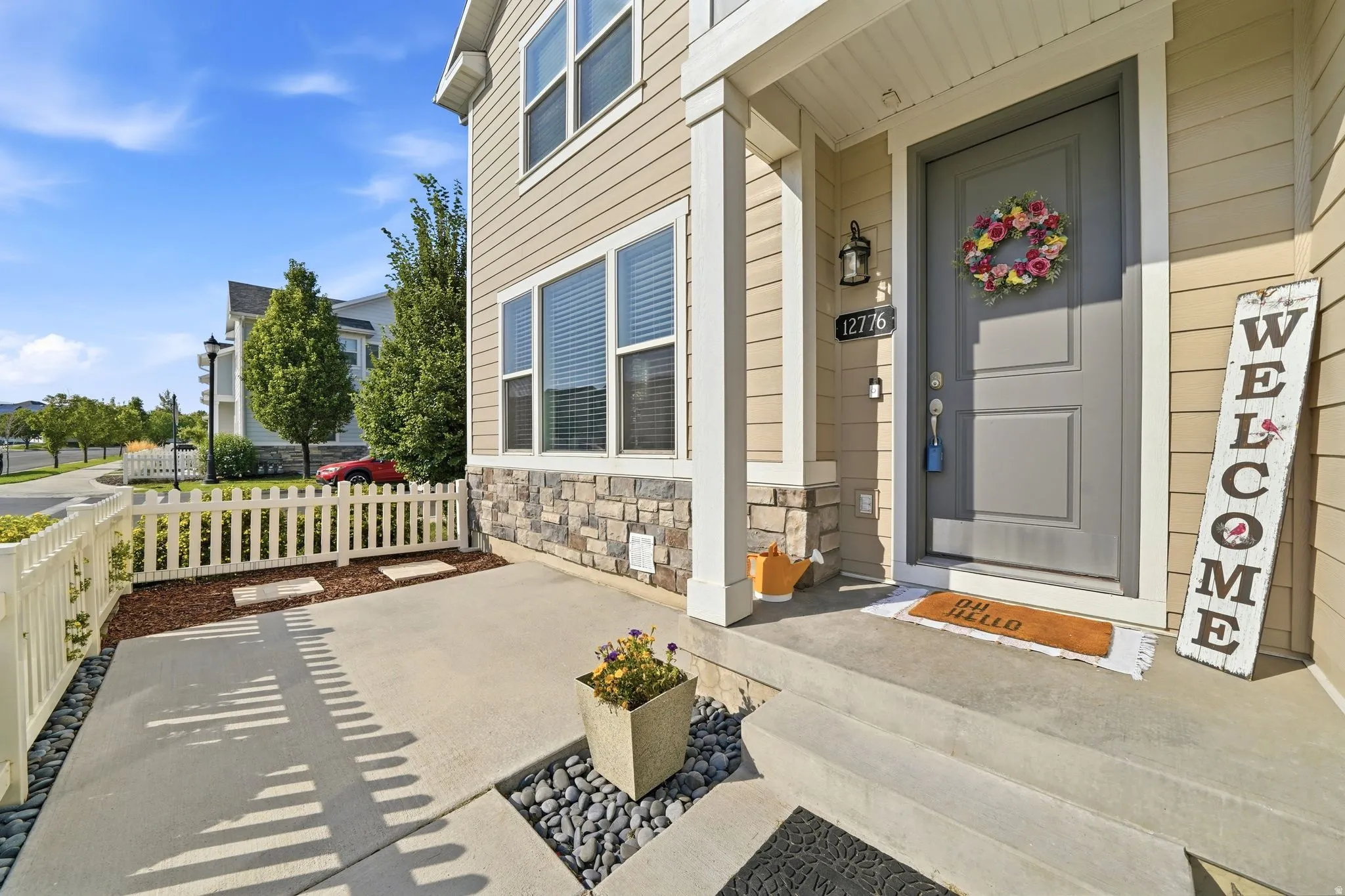 Siding exterior with stone veneer accents, concrete patio, white picket fence, and a gray panel front door