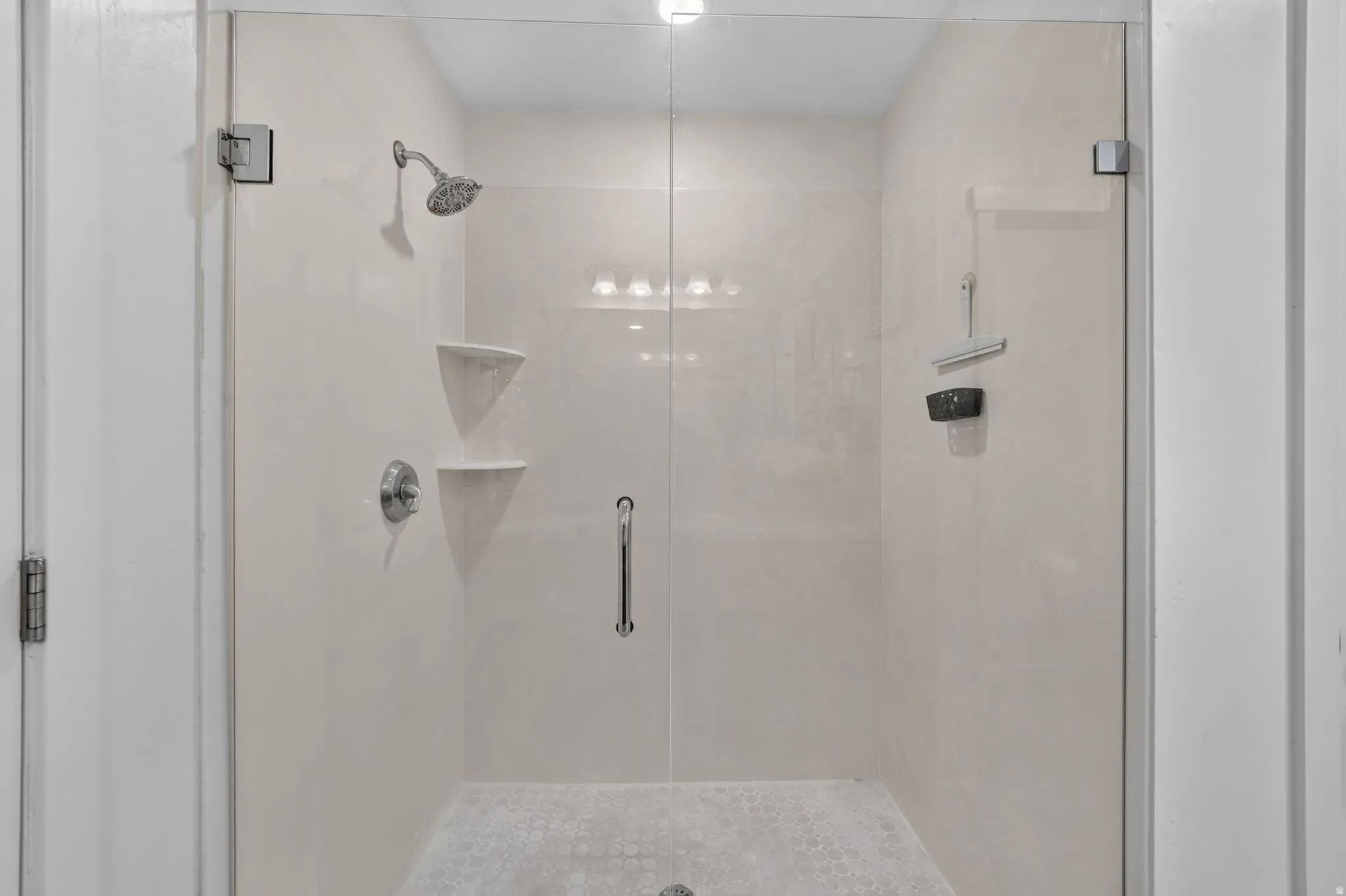 Glass-enclosed shower with a rainfall showerhead, integrated shelving, and a patterned tile floor