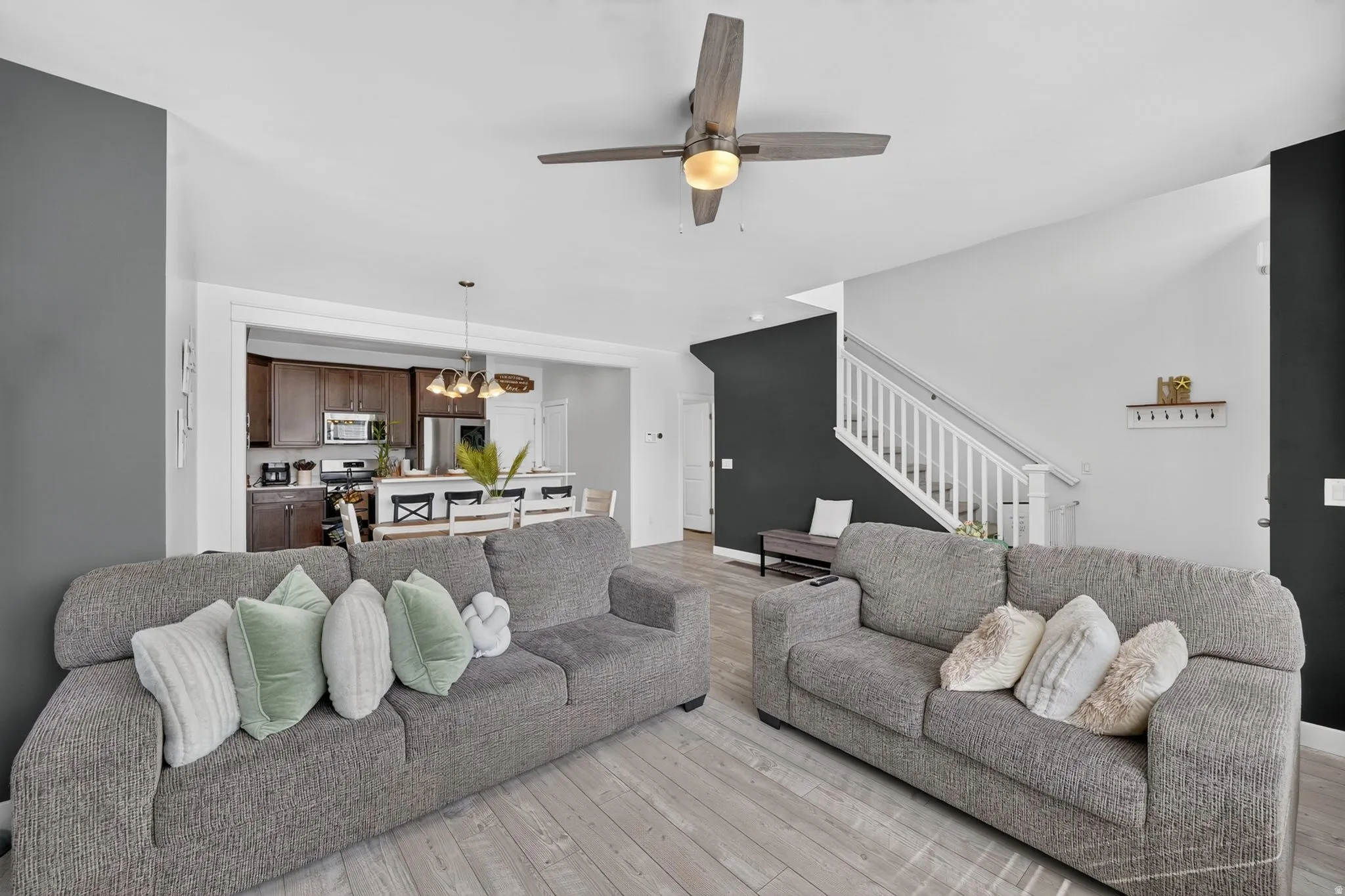 Open-concept living area with wood-finish flooring, a ceiling fan with integrated lighting, and a white staircase with balusters