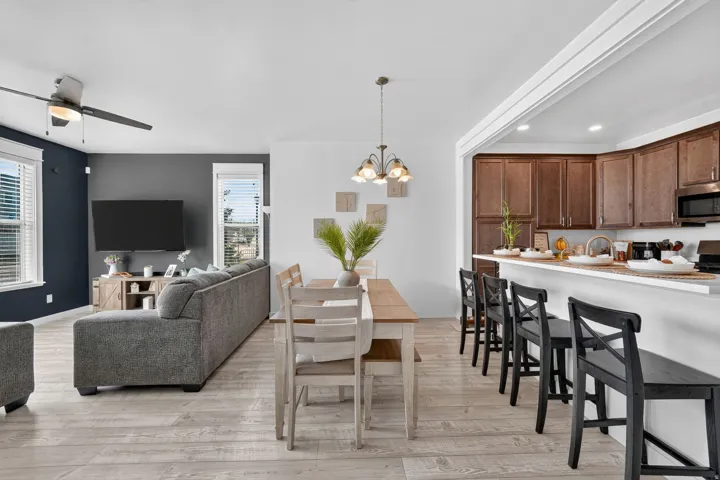 Open-concept layout featuring wood-finish flooring, a ceiling fan, and a kitchen with a breakfast bar