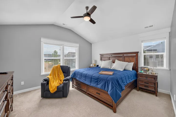 Vaulted ceiling with a ceiling fan, carpeted flooring, and multiple windows with blinds
