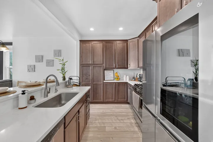 Kitchen featuring wood-finish flooring, stainless steel appliances, a stainless steel sink with a gooseneck faucet, white countertops, and wood cabinetry