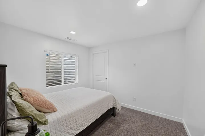 Recessed ceiling lighting, white walls, white window blinds, and dark gray carpet