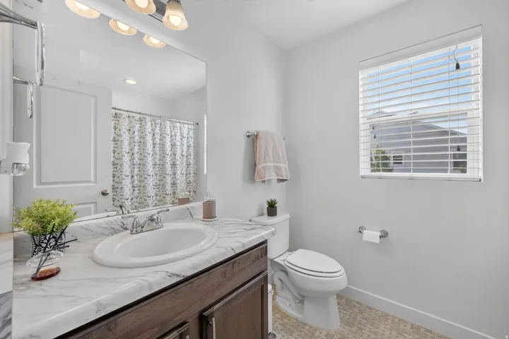 Bathroom featuring a wood-finish vanity with a white countertop and integrated sink, a large wall-mounted mirror, and a window with blinds