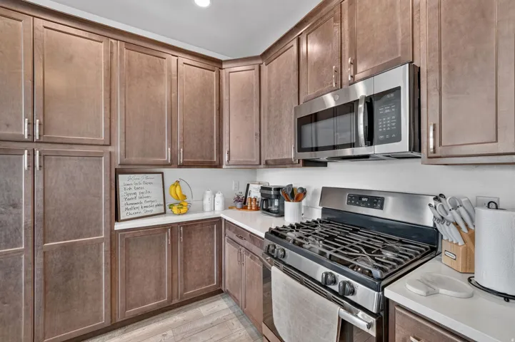 Kitchen featuring wood-finish cabinetry, stainless steel microwave, stainless steel gas range, and white countertops