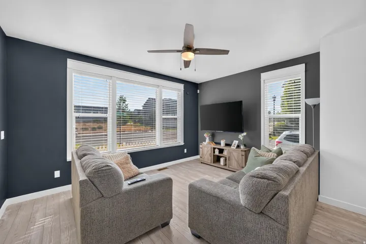 Expansive multi-pane window with white blinds, wood-finish flooring, dark accent wall, and a ceiling fan with integrated lighting