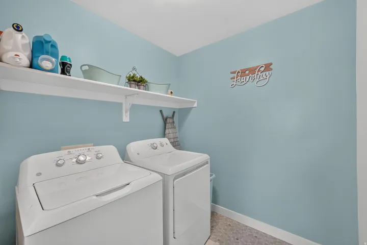 Integrated laundry appliances with upper storage shelving, light blue wall paint, and patterned floor tiling