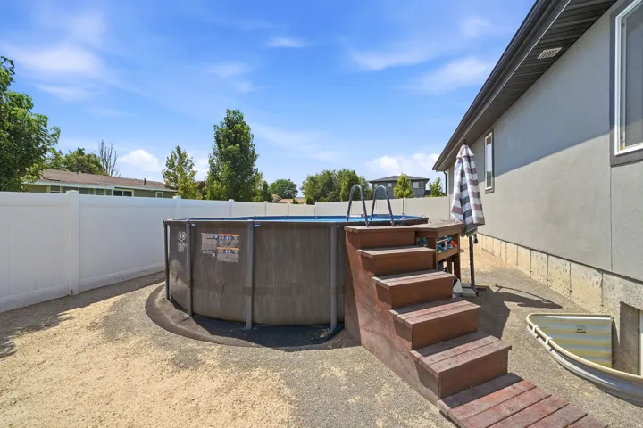 Above-ground pool with wood-finish access steps, surrounded by a white privacy fence