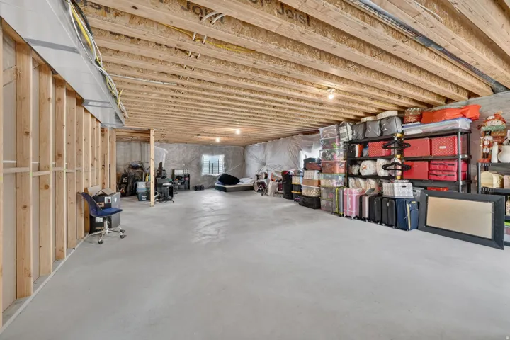 Expansive unfinished basement featuring exposed joists, concrete flooring, and ample storage space