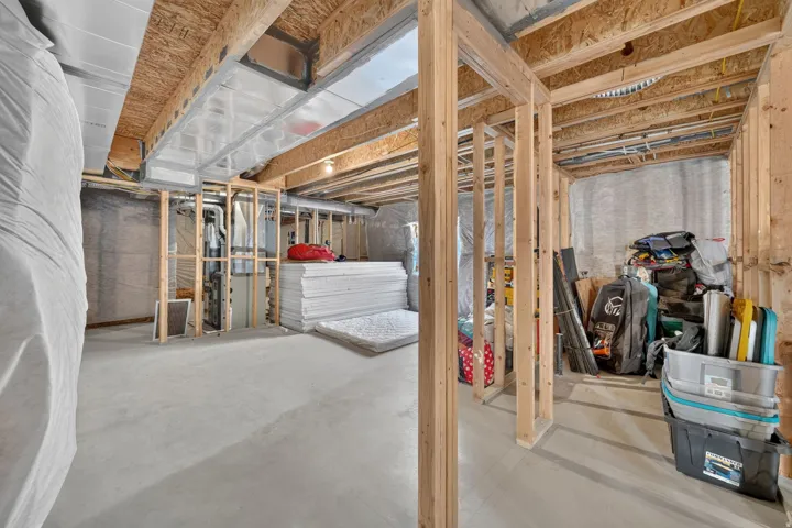 Unfinished basement featuring exposed wood joists, concrete flooring, and partial wood framing