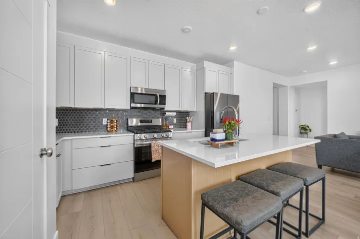 Contemporary kitchen featuring white shaker cabinetry, stainless steel appliances, a dark mosaic tile backsplash, and a light wood-finish island with a white countertop