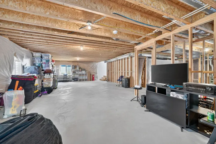 Unfinished basement with exposed ceiling joists and wood framing, featuring concrete flooring and a window