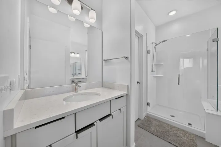 White vanity with a single basin sink and light-toned countertop, paired with a modern shower enclosure featuring a clear glass door