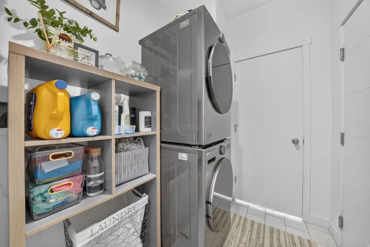 Utility area featuring a stacked washer and dryer, wood-finish shelving, and white tile flooring