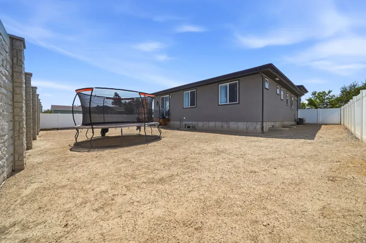 Spacious property featuring a stucco exterior, multiple windows, a white vinyl fence, and a stone-clad perimeter wall