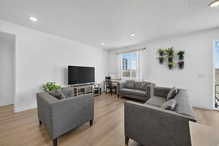 Recessed ceiling lighting, light wood-finish flooring, white walls, and a large window with white curtains