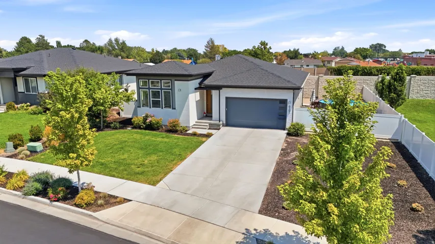 Contemporary single-story residence with a gray garage door, concrete driveway, manicured lawn, and mature landscaping